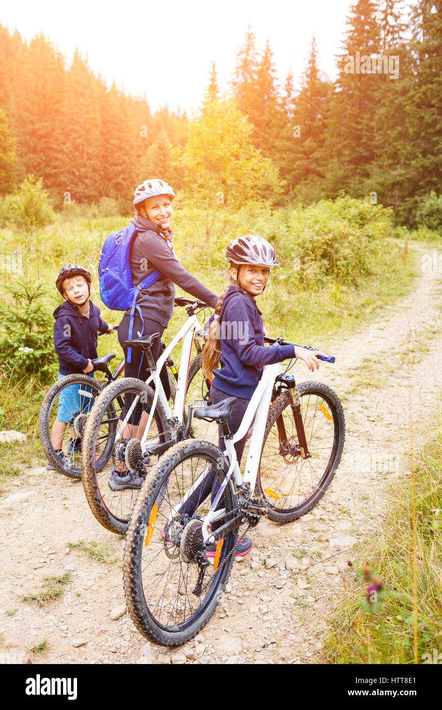 Young girl with her mother and small brother enjoying cycling in forest. Family riding bike concept background Stock Photo