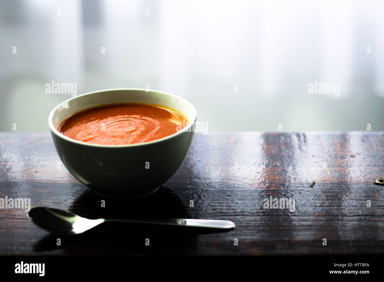 Picture of a bawl of tomato soup with a spoon on the side sitting on a wooden board Stock Photo