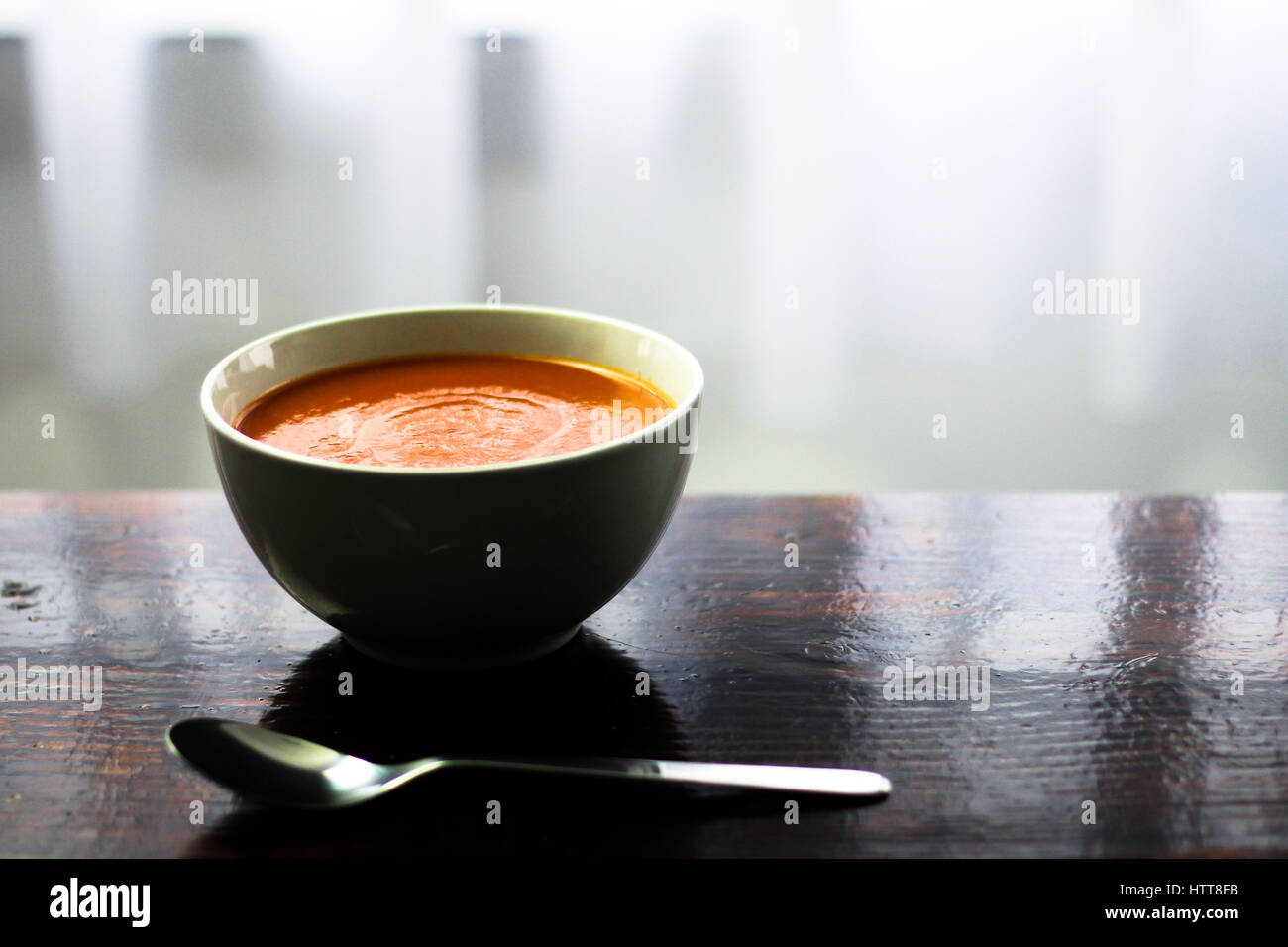 Picture of a bawl of tomato soup with a spoon on the side sitting on a wooden board Stock Photo