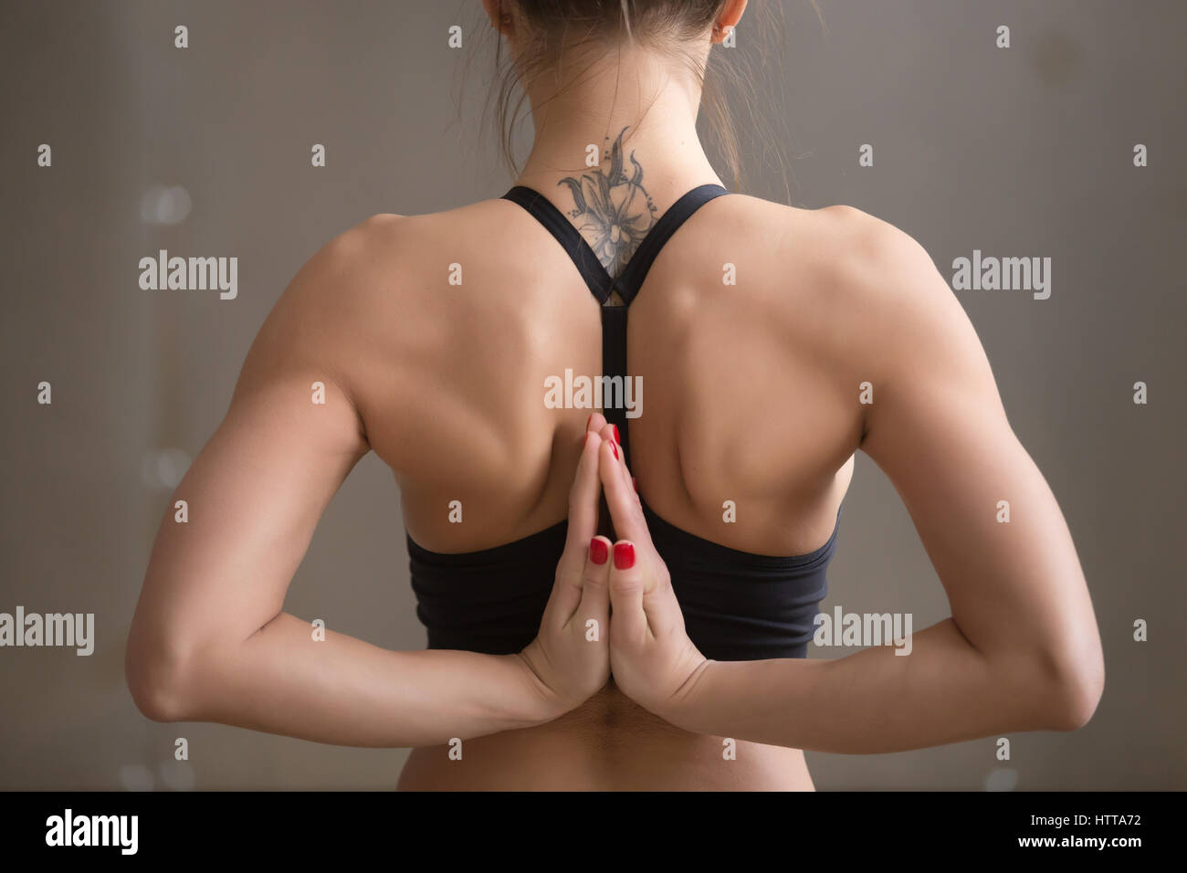 Young attractive woman making Namaste behind the back, grey stud Stock Photo