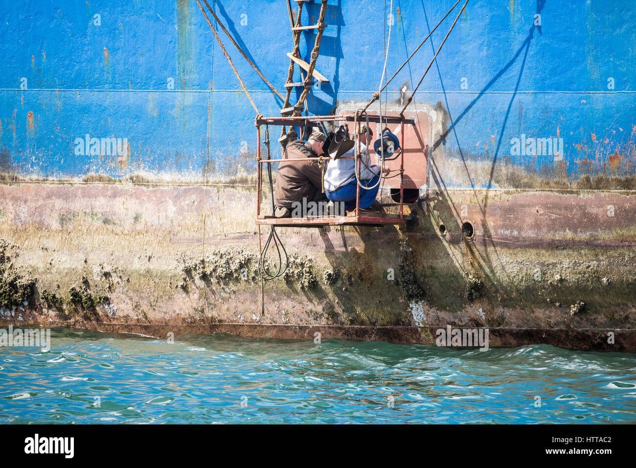 Welder working from makeshift platform repairing rusting Russian trawler im Las Palmas port on Gran Canaria. Stock Photo