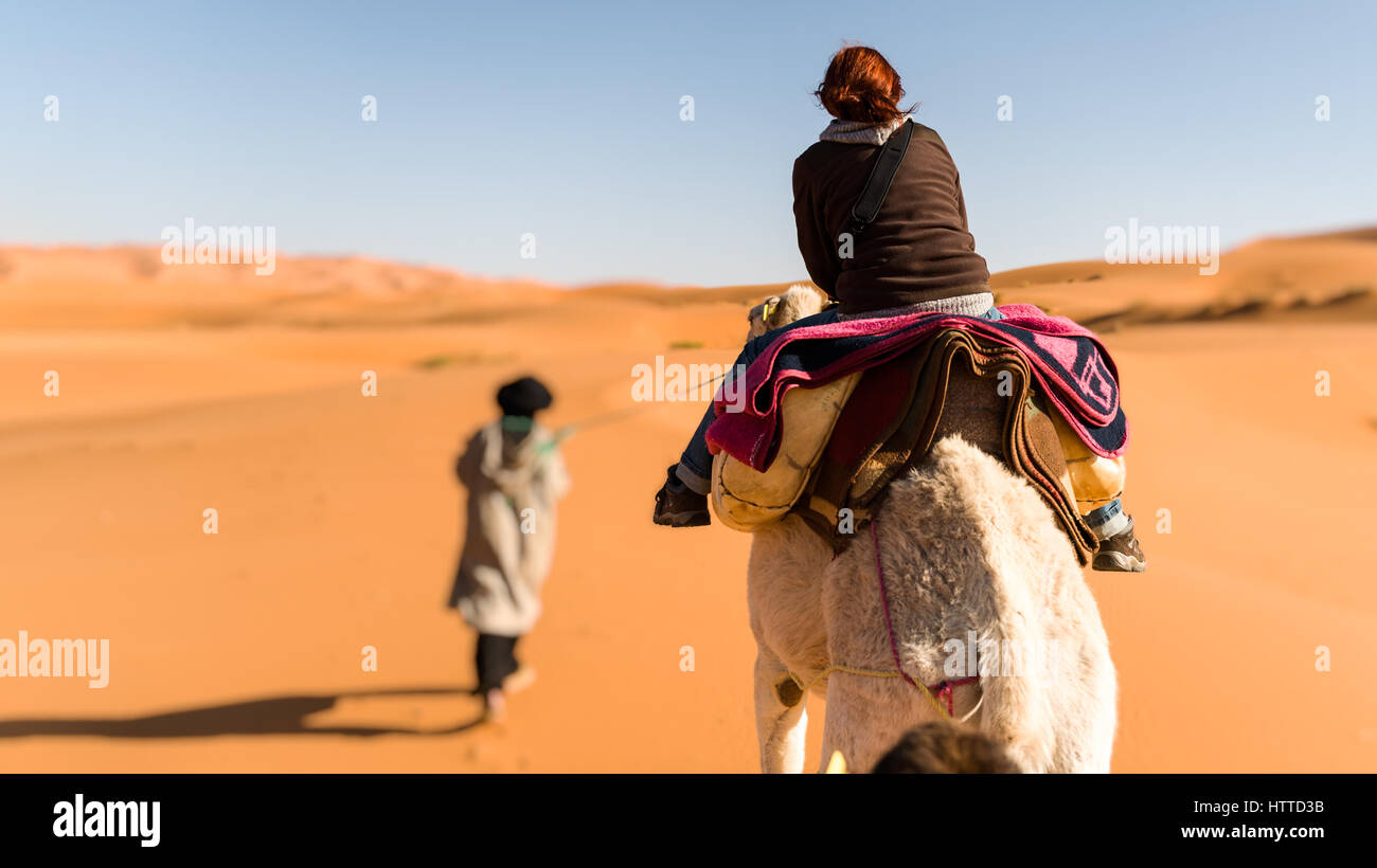 Woman traveling on camel led by a berber nomad, back view Stock Photo