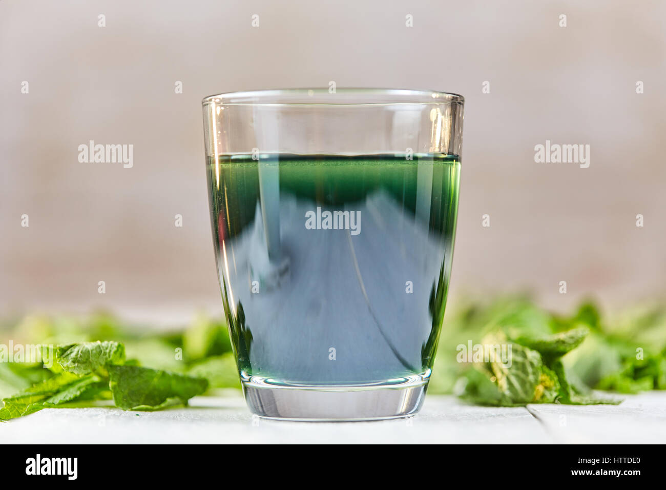 Green chlorophyll drink in glass with water on white table with green