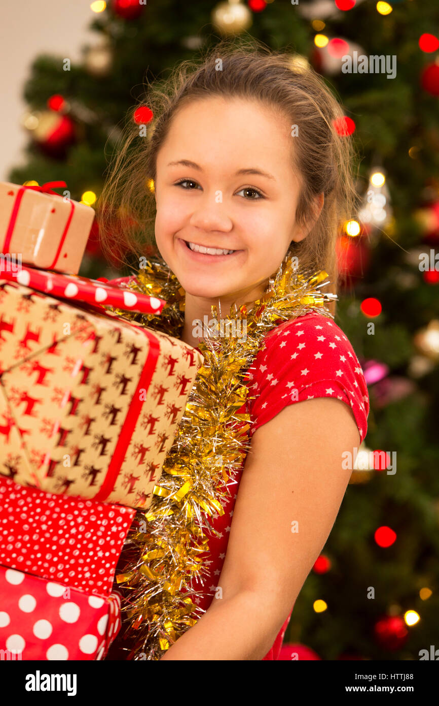 A teenage girl is carrying a pile of Christmas presents, while smiling at the camera. Stock Photo