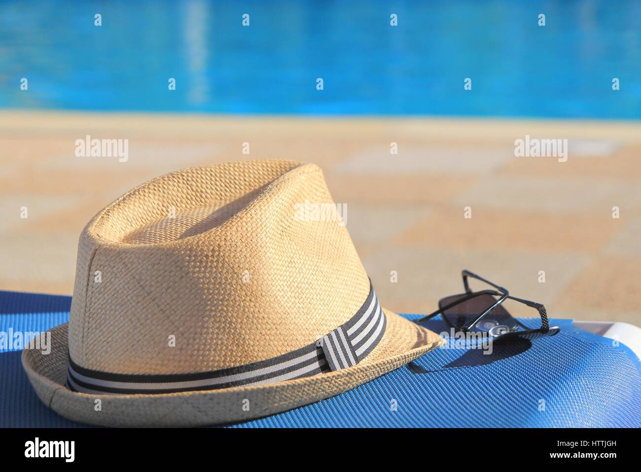 Straw hat and sunglasses on a poolside sunlounger in early morning ...