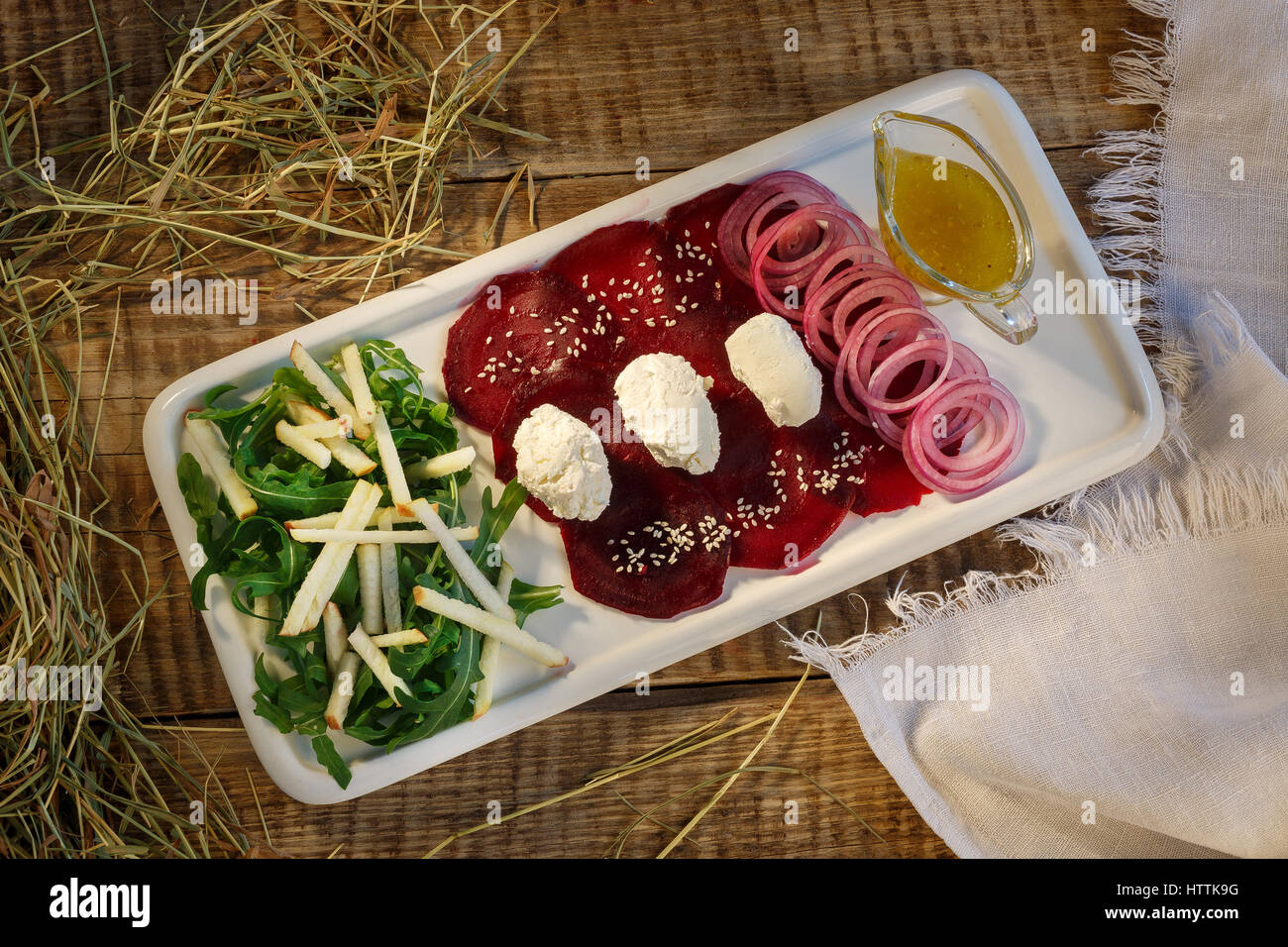 Red beet, greend, rings of onions with yellow cream and pastry, tastya white souce cream served on white plate standing on wooden table in exclusive f Stock Photo