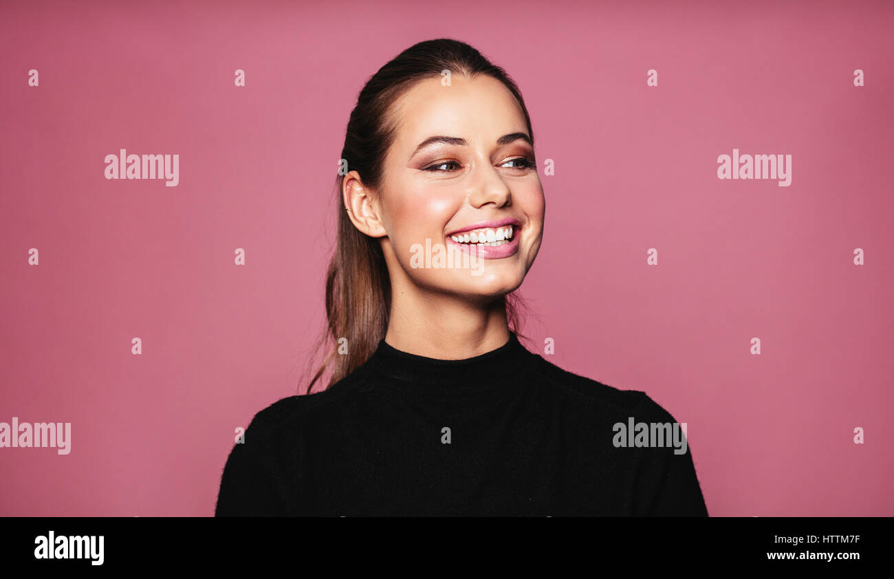 Portrait of caucasian female model standing and smiling against pink background. Beautiful woman with perfect skin and makeup looking away. Stock Photo