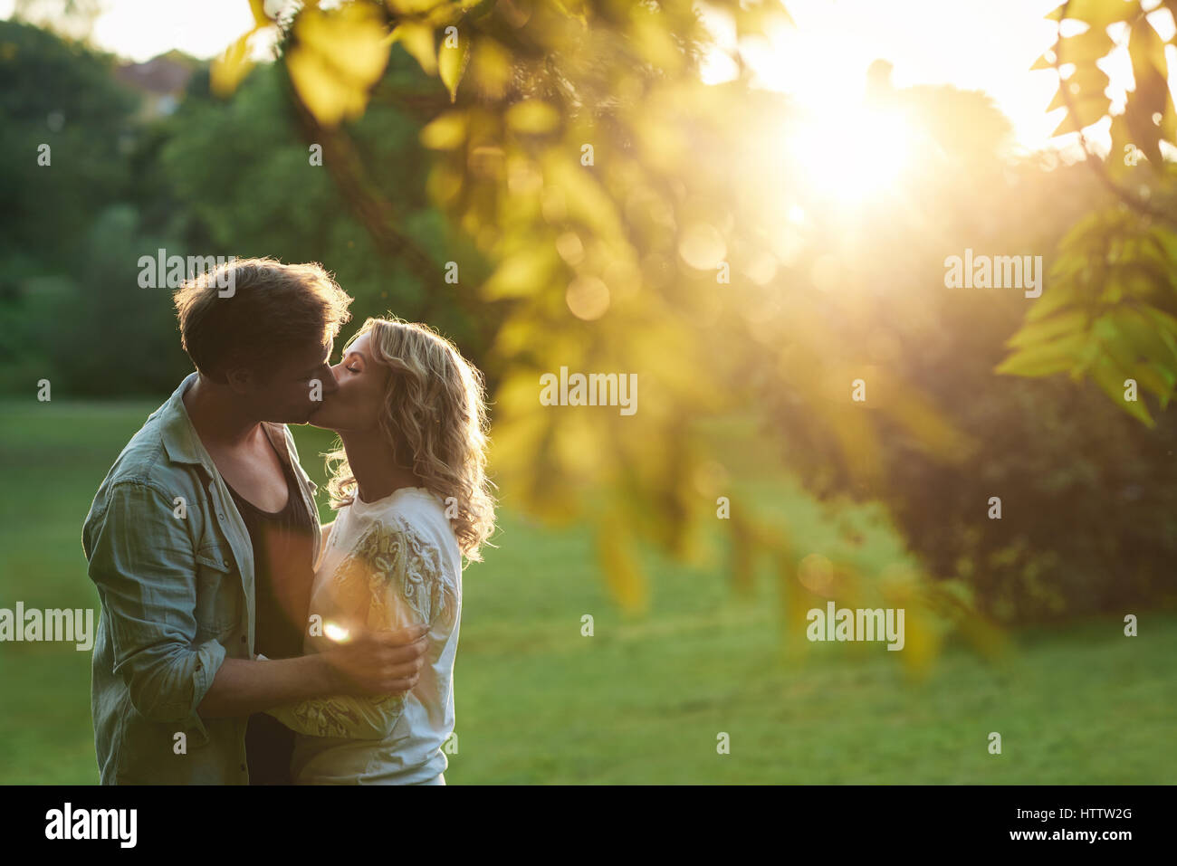 Affectionate young couple kissing each other with their eyes closed while enjoying a romantic sunny summer afternoon together in a park Stock Photo