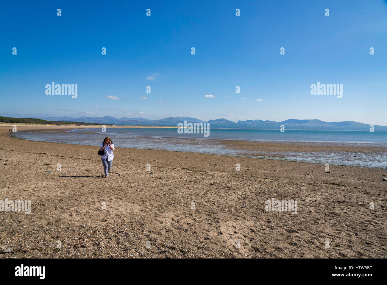 Woman using a mobile phone on a deserted beach on Llanddwyn Island (Ynys Llanddwyn). Anglesey North Wales. Stock Photo