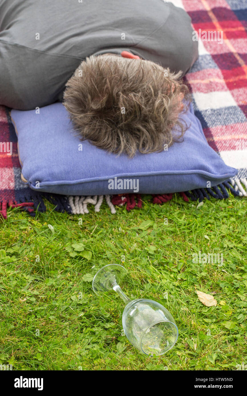 Man lying down in garden sleeping with fallen empty wine glass in grass Stock Photo