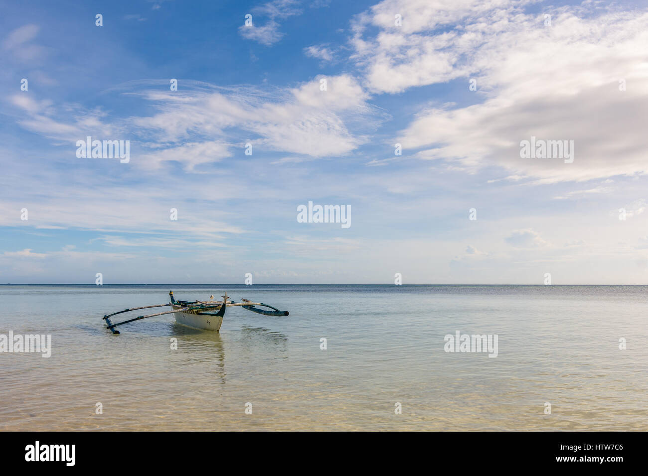 Traditional Filipino fishing boat with seagulls on the outriggers floating in a calm sea. Stock Photo
