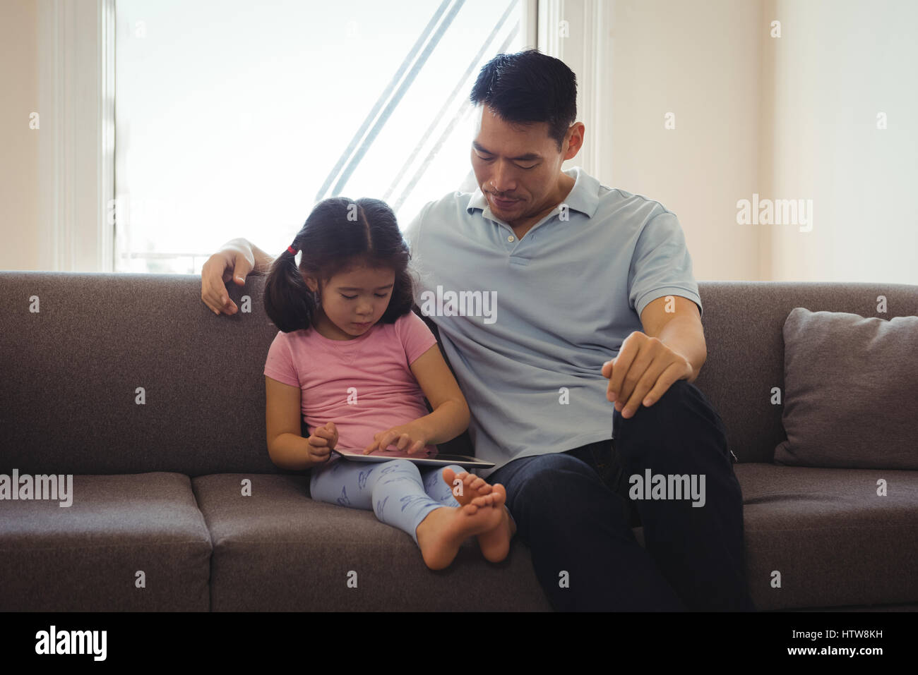 Father and daughter using digital tablet in living room Stock Photo