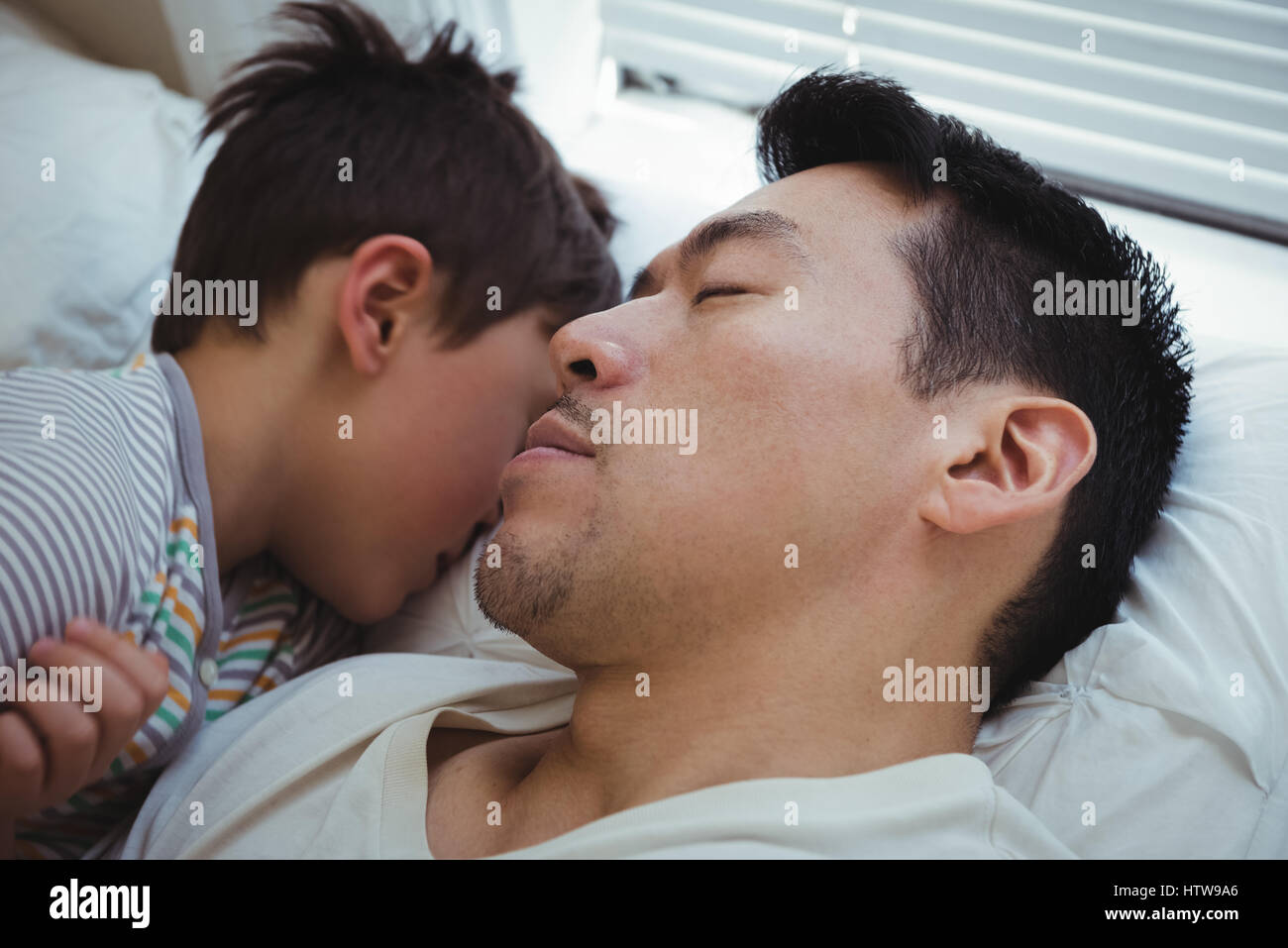 Father and son sleeping together in bedroom Stock Photo