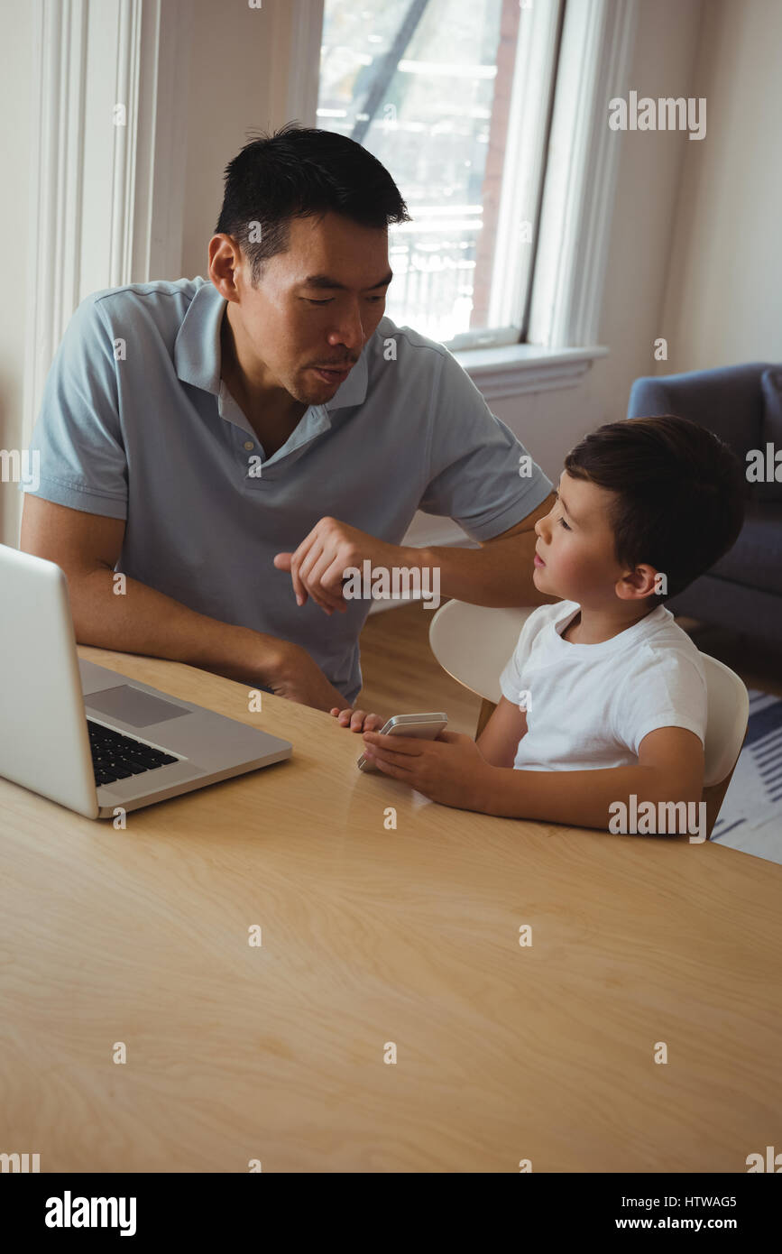 Father and son using mobile phone and laptop in living room Stock Photo