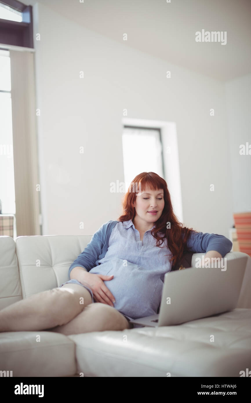Pregnant Woman Using Laptop While Relaxing On Sofa In Living Room