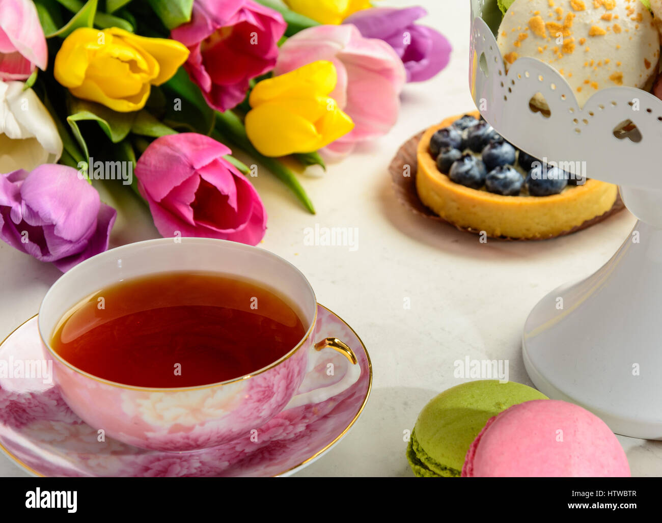 Beautiful festive bouquet of tulips, cakes and cup of tea on white background. Stock Photo