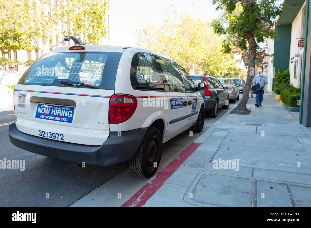 United States Postal Service vehicle with sign reading Now Hiring, and postal carrier walking towards the vehicle, in the Silicon Valley town of Palo Alto, California, August 25, 2016. Stock Photo