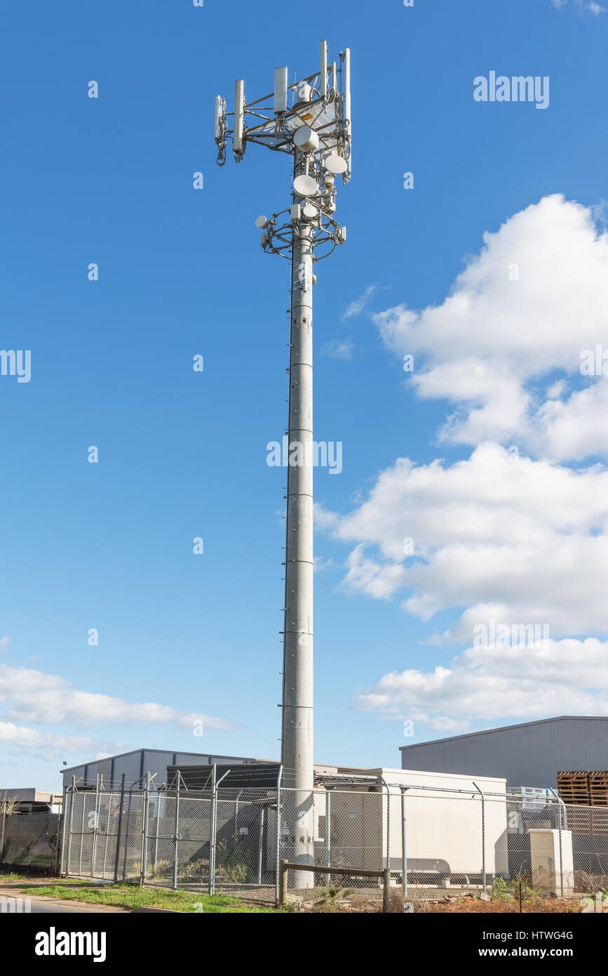 Communications Cell phone Tower against blue sky near industry buildings Stock Photo