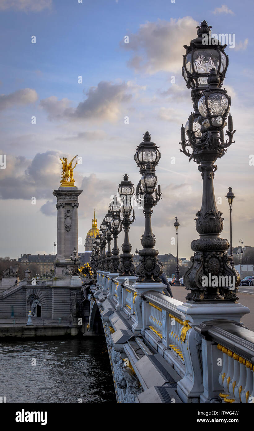 Lights along the Pont Alexandre III bridge over the Seine river in Paris, France.  View looking toward Musee de L'Armee with ornate gold statues. Stock Photo