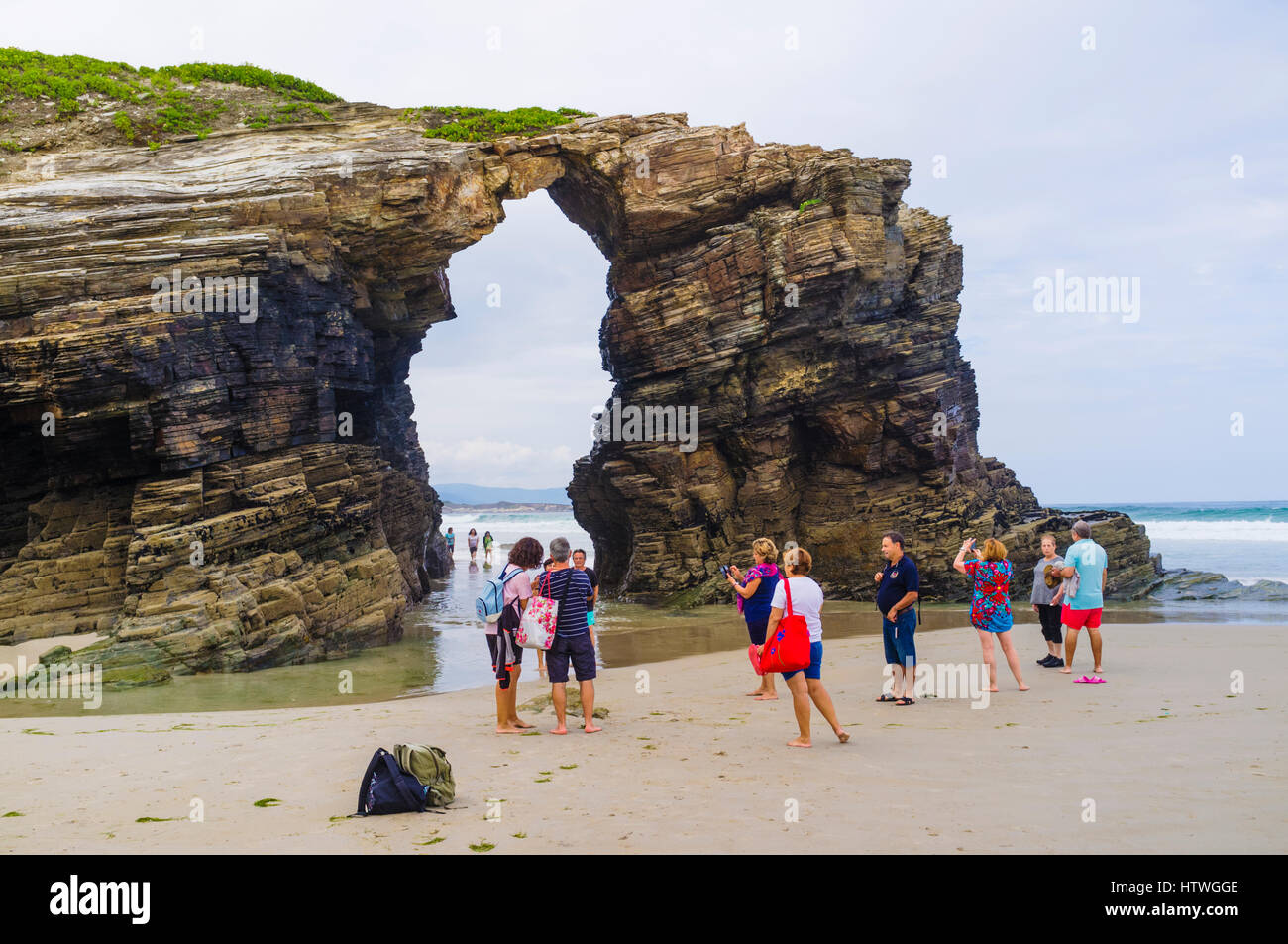 Group of tourists by a stone arch at Beach of the Cathedrals Natural Monument at Ribadeo municipality, Lugo province, Galicia, Spain, Europe Stock Photo