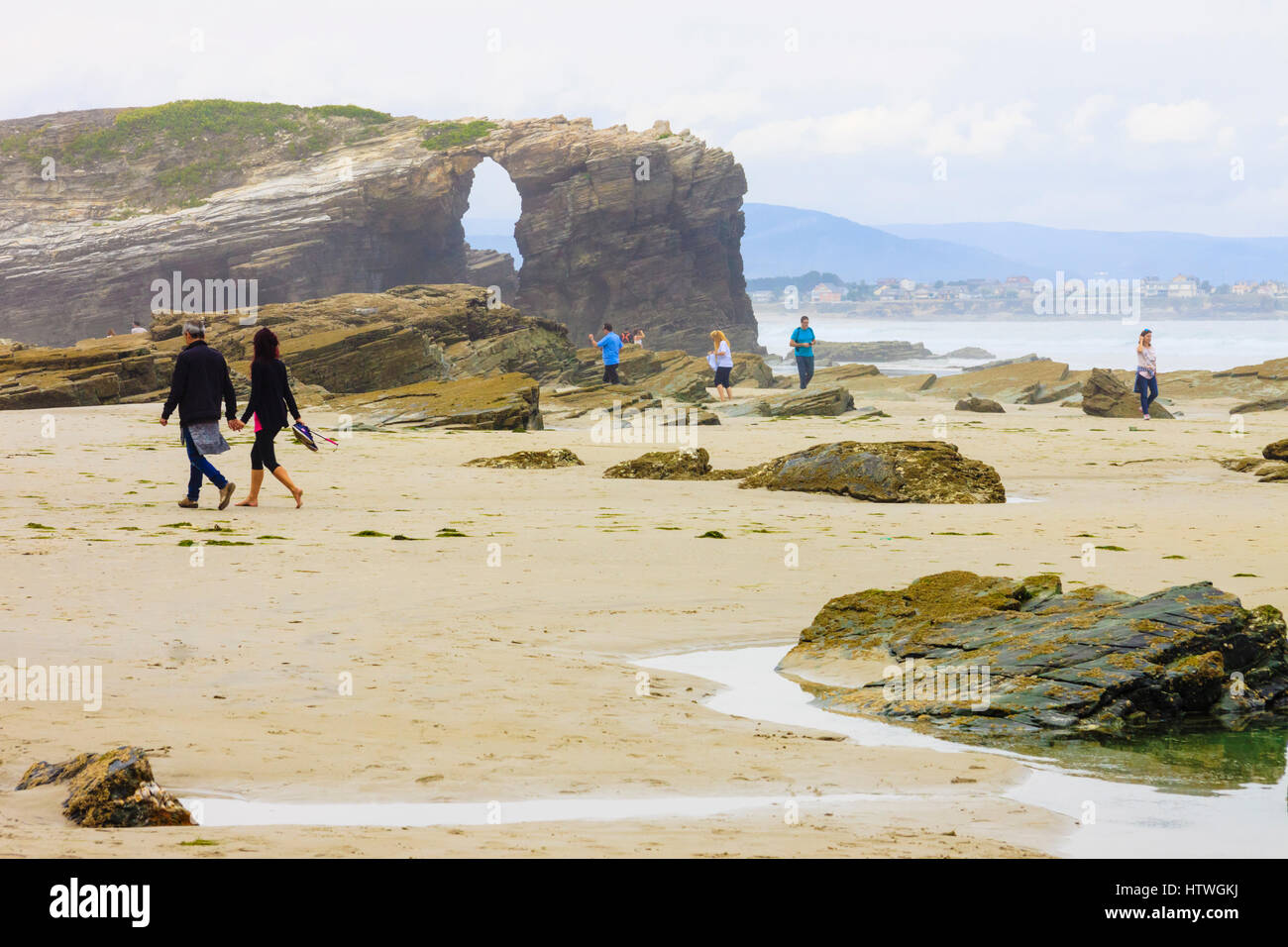 Tourists by a stone arch at Beach of the Cathedrals Natural Monument at Ribadeo municipality, Lugo province, Galicia, Spain, Europe Stock Photo