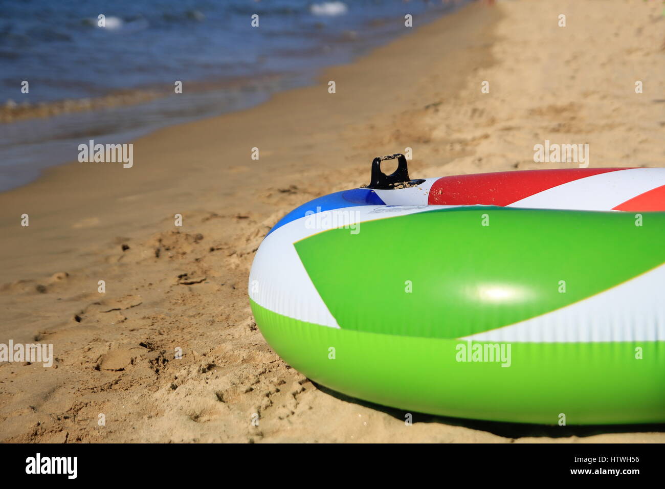 Colorful inflatable ring on a beautiful sandy beach in the summer sunshine, green, red, white, blue. Stock Photo