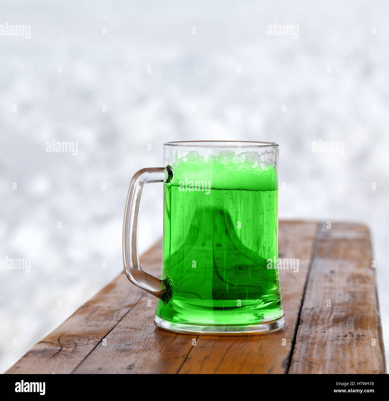 St. Patricks Day. Full fresh cold glass of green beer on wooden bench. Stock Photo