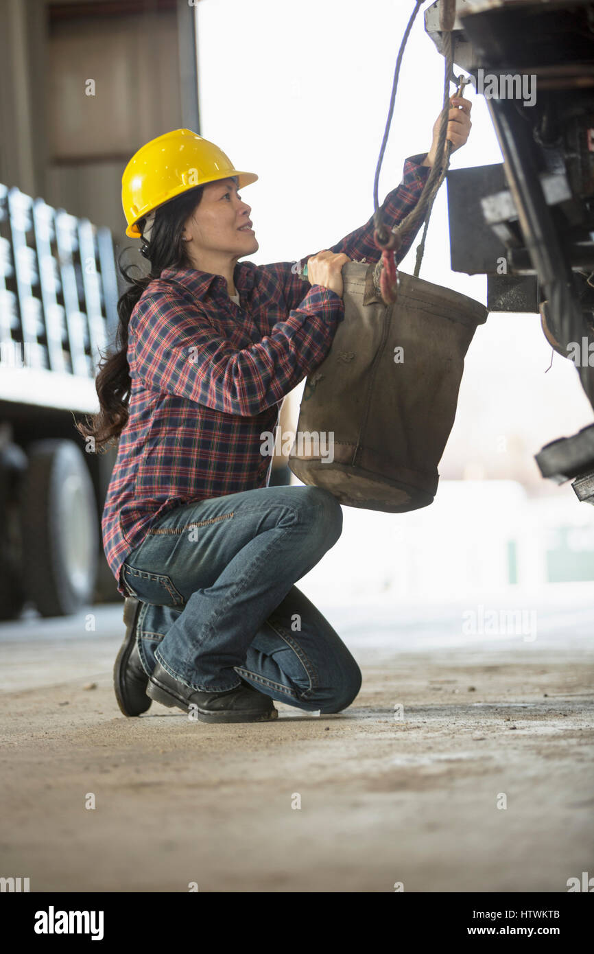 Female power engineer attaching canvas bucket to equipment truck Stock Photo