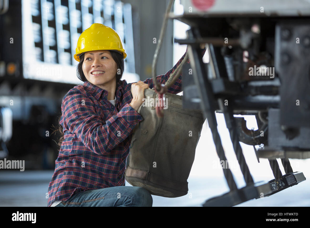 Female power engineer attaching canvas bucket to equipment truck Stock Photo