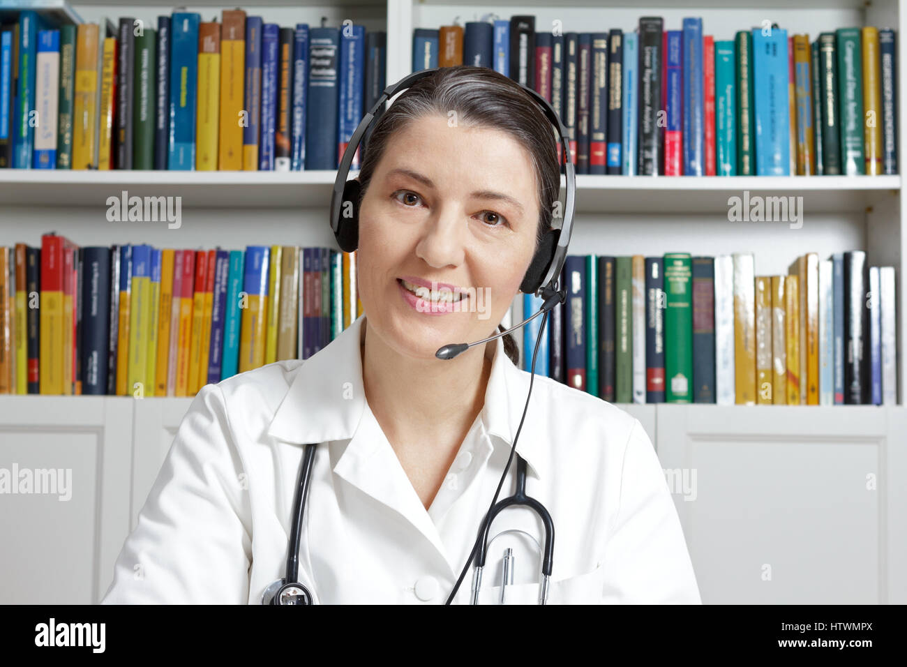 Friendly doctor or general practitioner with headset in surgery office in a live chat with a patient, as seen through a webcam, online medical consult Stock Photo