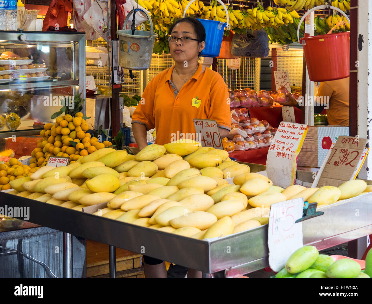 A Singaporean shopkeeper selling fruit, predominantly mangoes and bananas, at a fruit shop. Stock Photo