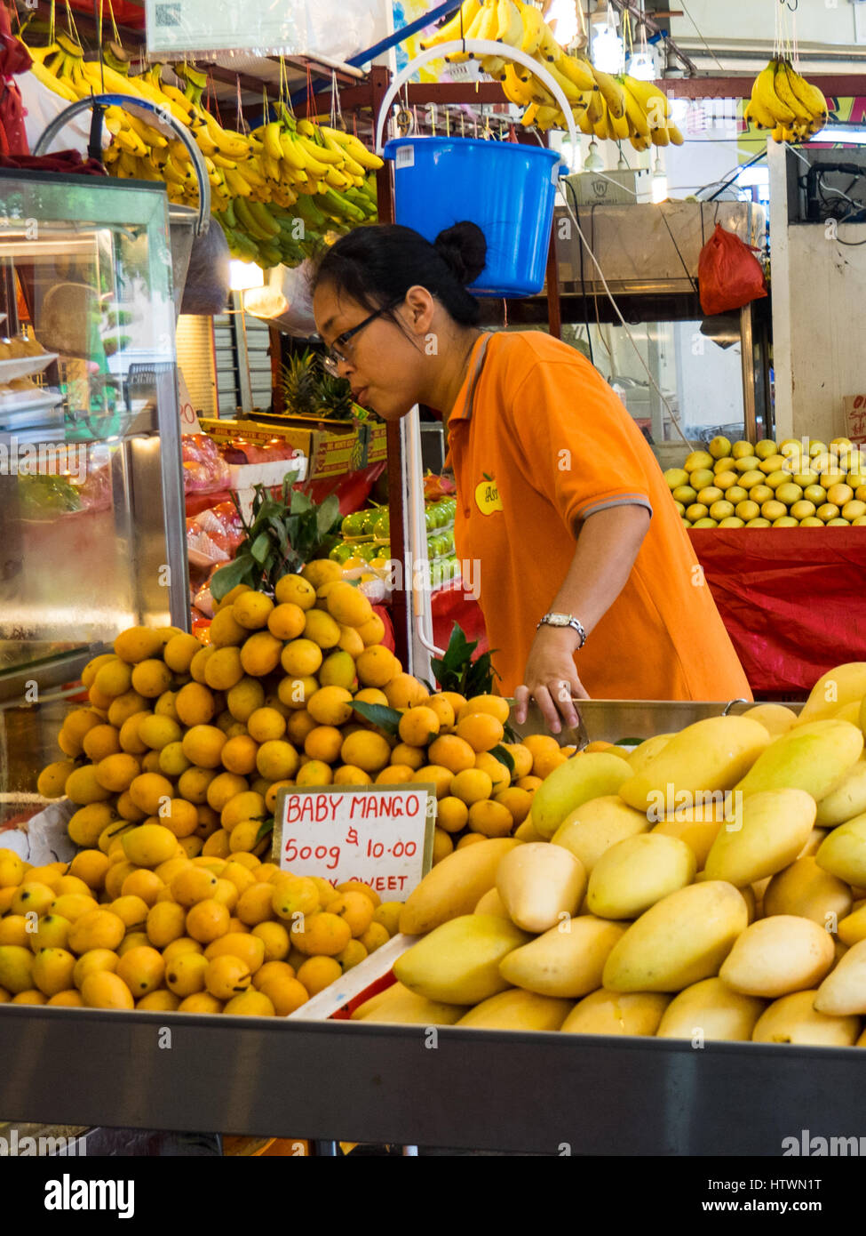 A Singaporean shopkeeper selling fruit, predominantly mangoes and bananas, at a fruit shop. Stock Photo