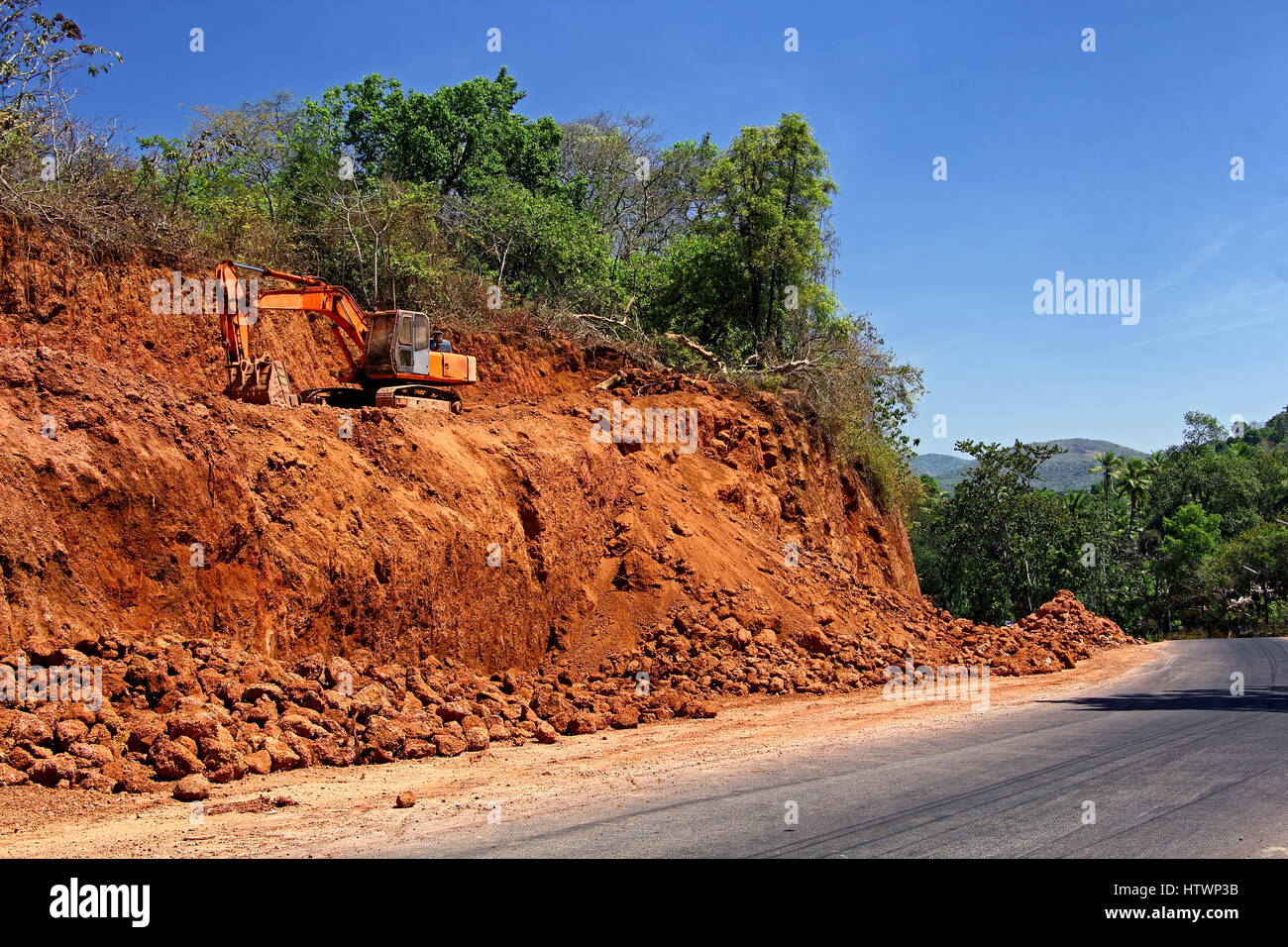 Massive earth cutting using heavy construction and earthmoving hydraulic equipment being done for widening highway in a hilly terrain Stock Photo