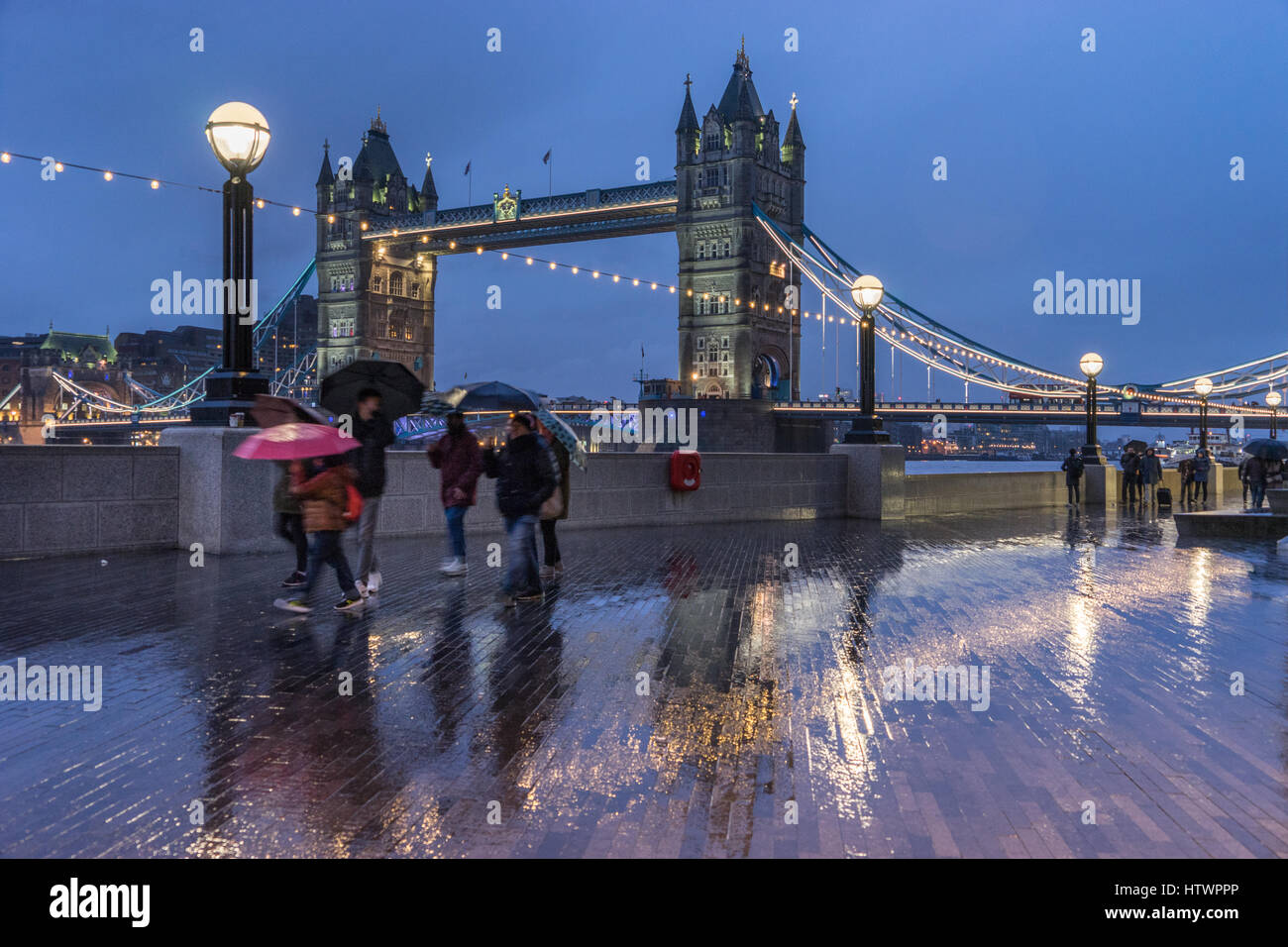 Family with umbrellas in rain rushing by with views of Tower Bridge