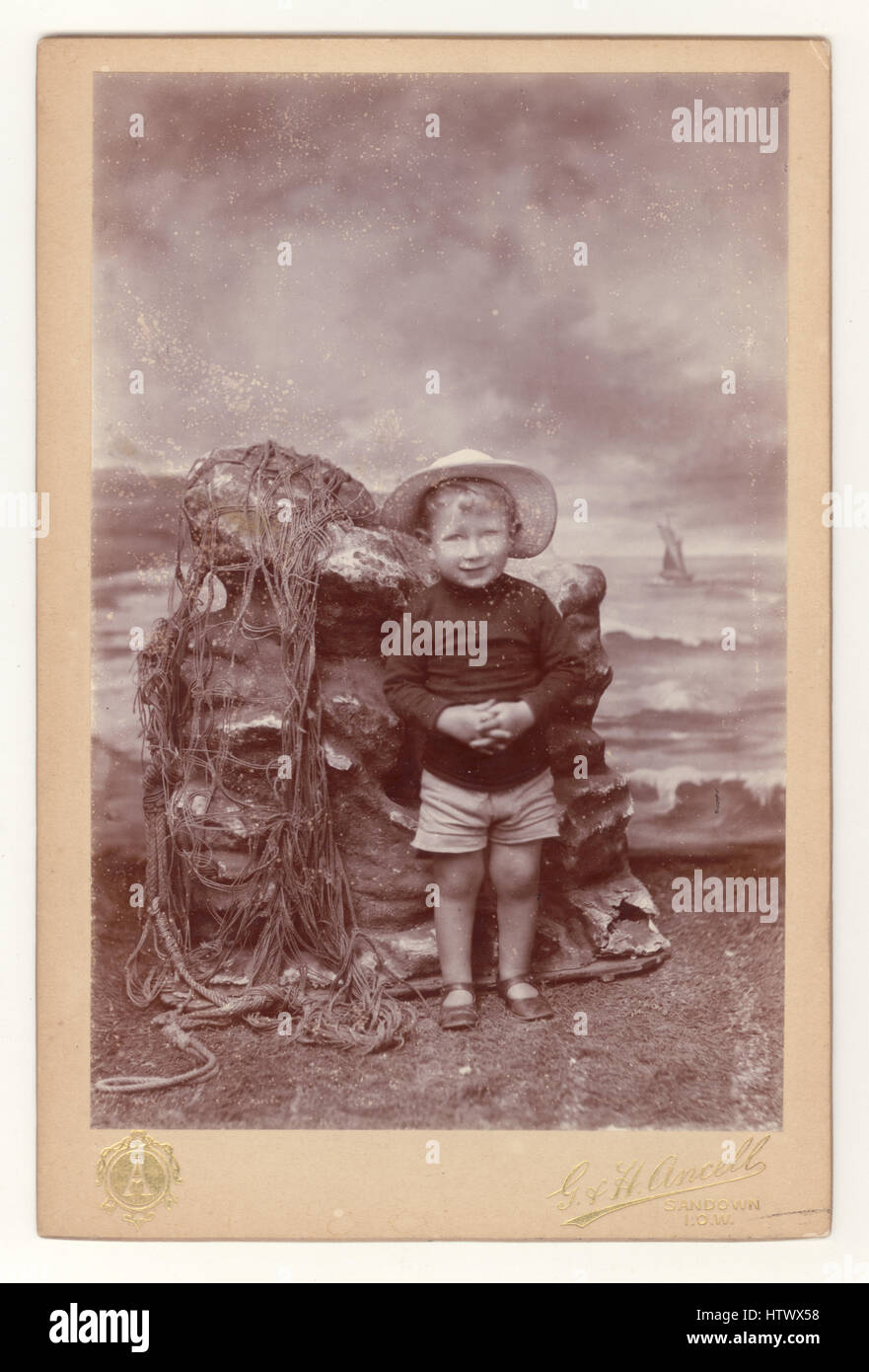 Original Edwardian cabinet card of a young child posing in a photographic studio with an elaborate seaside themed background / backdrop, Sandown, Isle of Wight, U.K. dated September 1909 Stock Photo