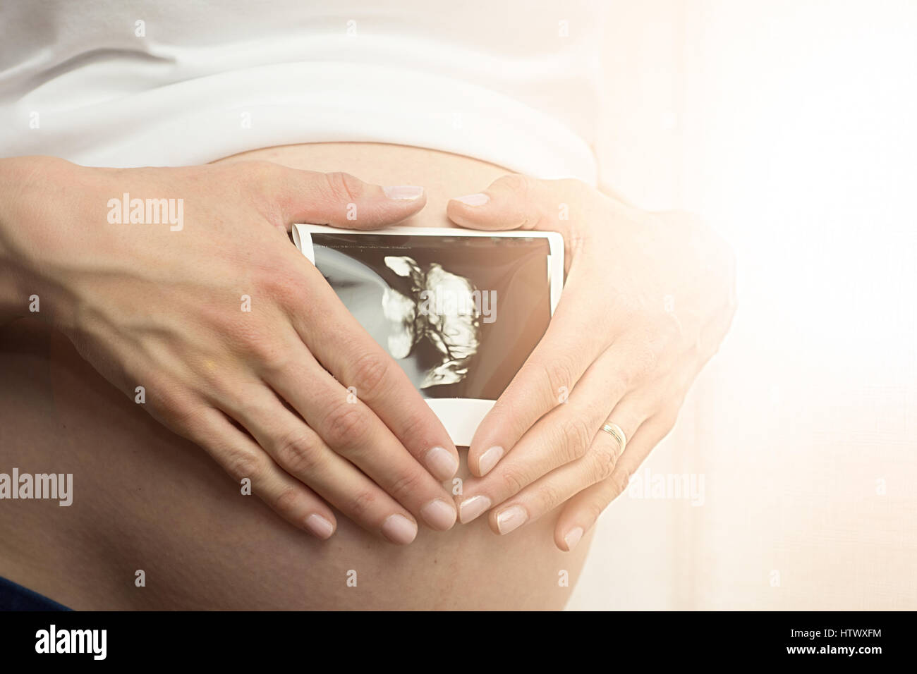 Pregnant woman holding ultrasound scan on her tummy. Stock Photo