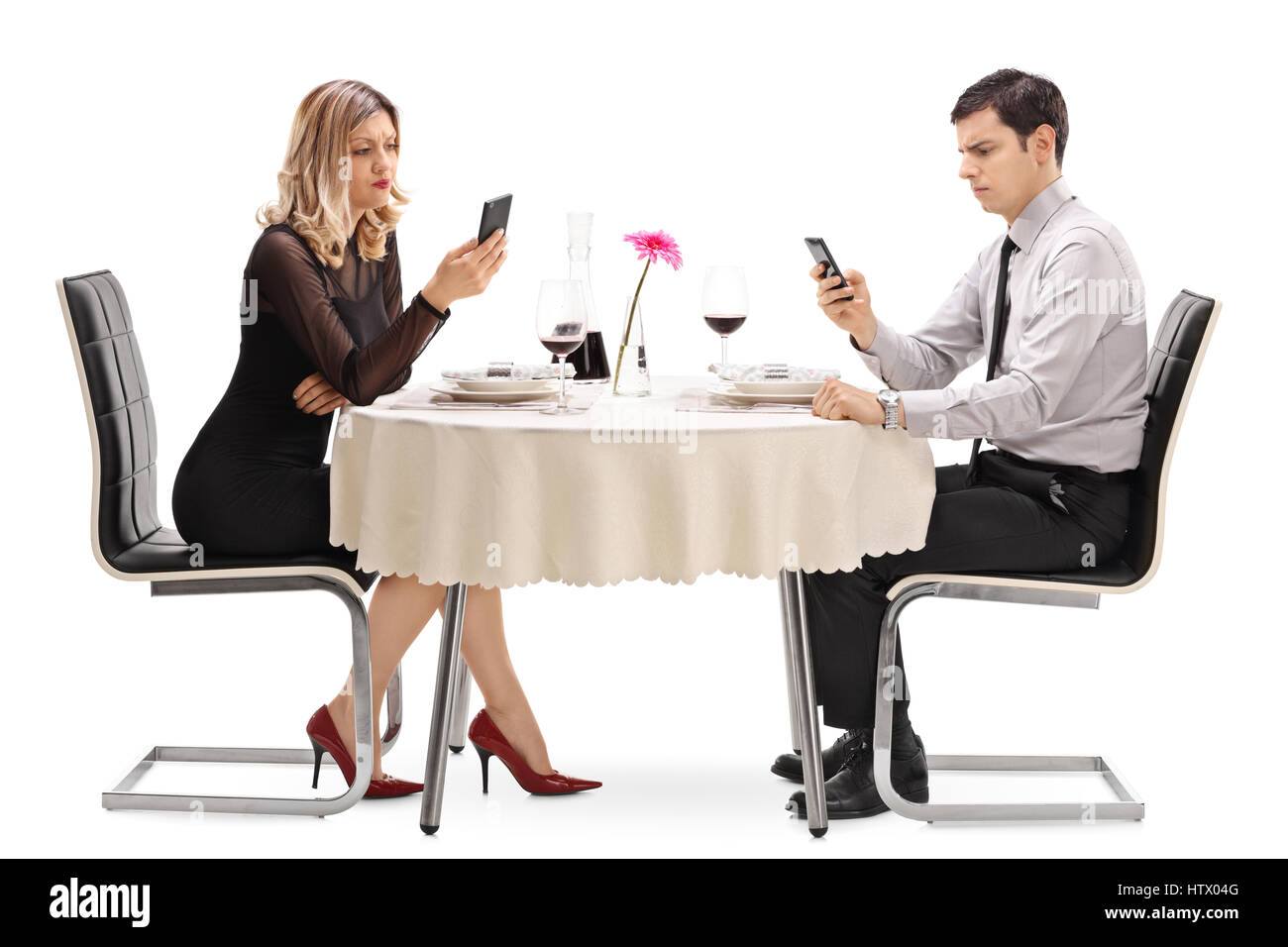 Young man and woman sitting at a restaurant table and looking at their phones isolated on white background Stock Photo