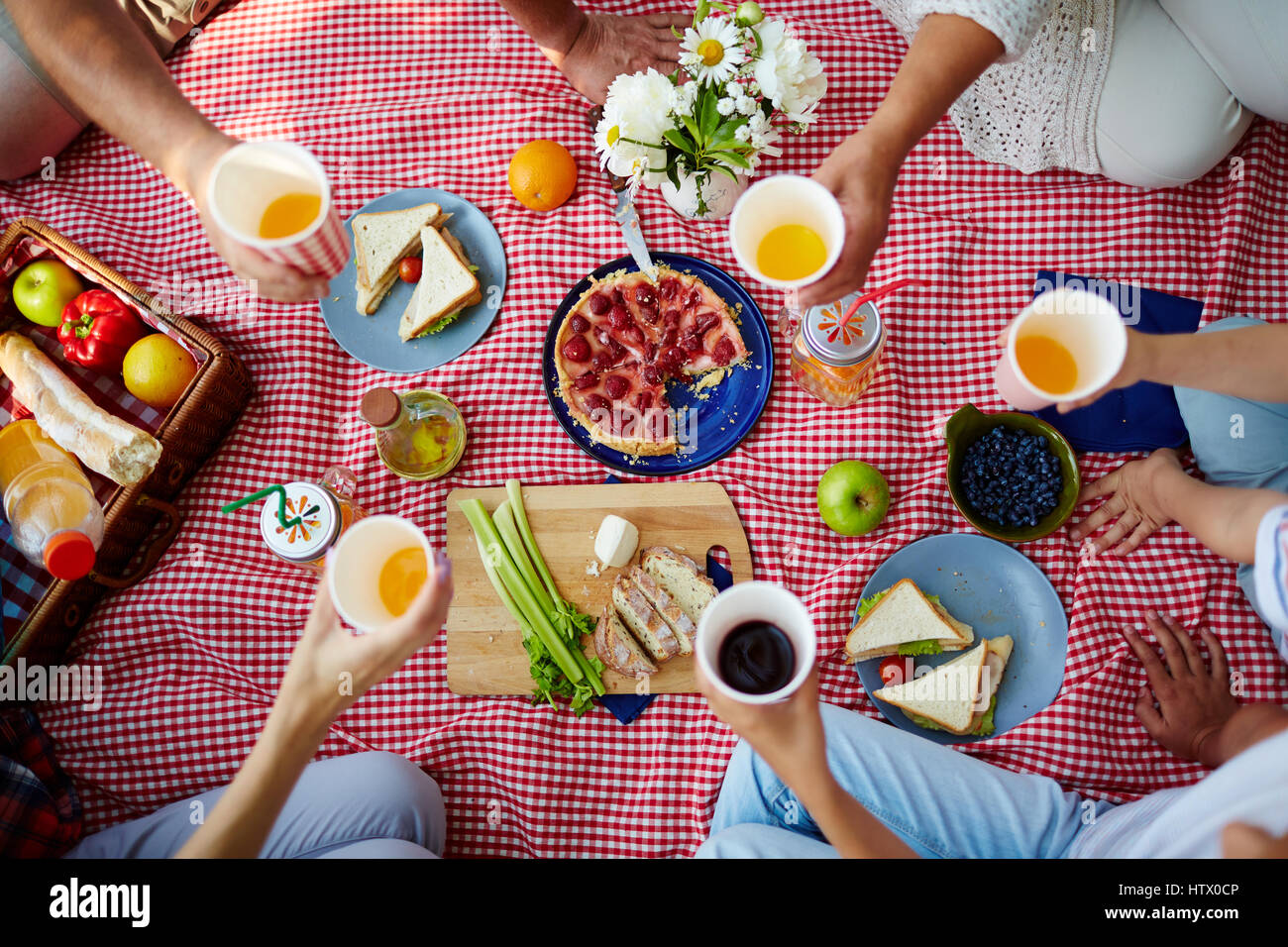 Picnic blanket with healthy food and human hands with drinks over it Stock Photo