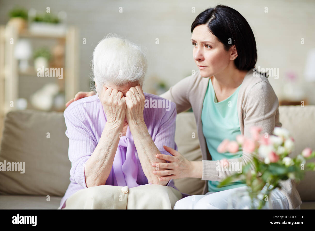 Crying senior female hiding her face with daughter near by Stock Photo