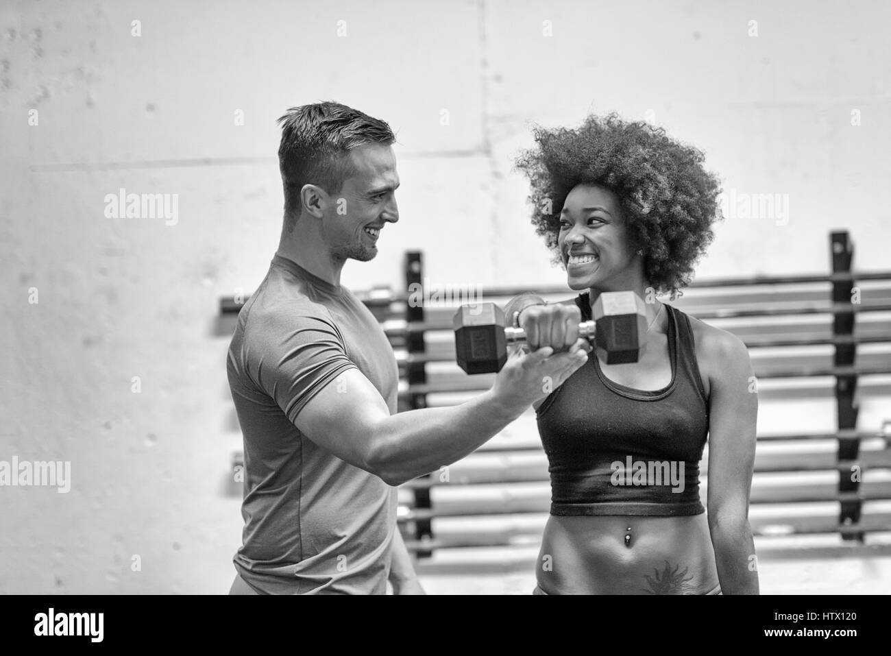 young beautiful African American woman doing bicep curls with fitness trainer in a gym Stock Photo