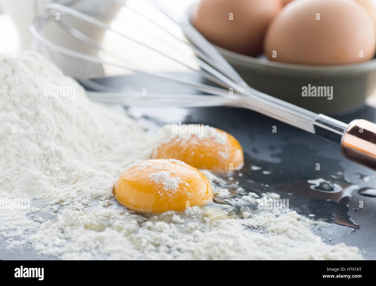 two cracked eggs showing yellow yolk on a pile of white flour with a