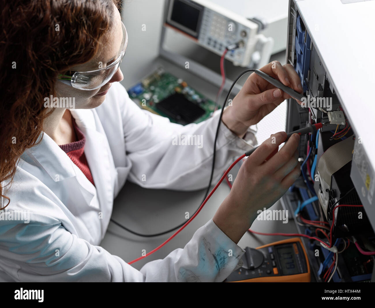 Engineer with white lab coat and goggles measures current with a meter, Austria Stock Photo