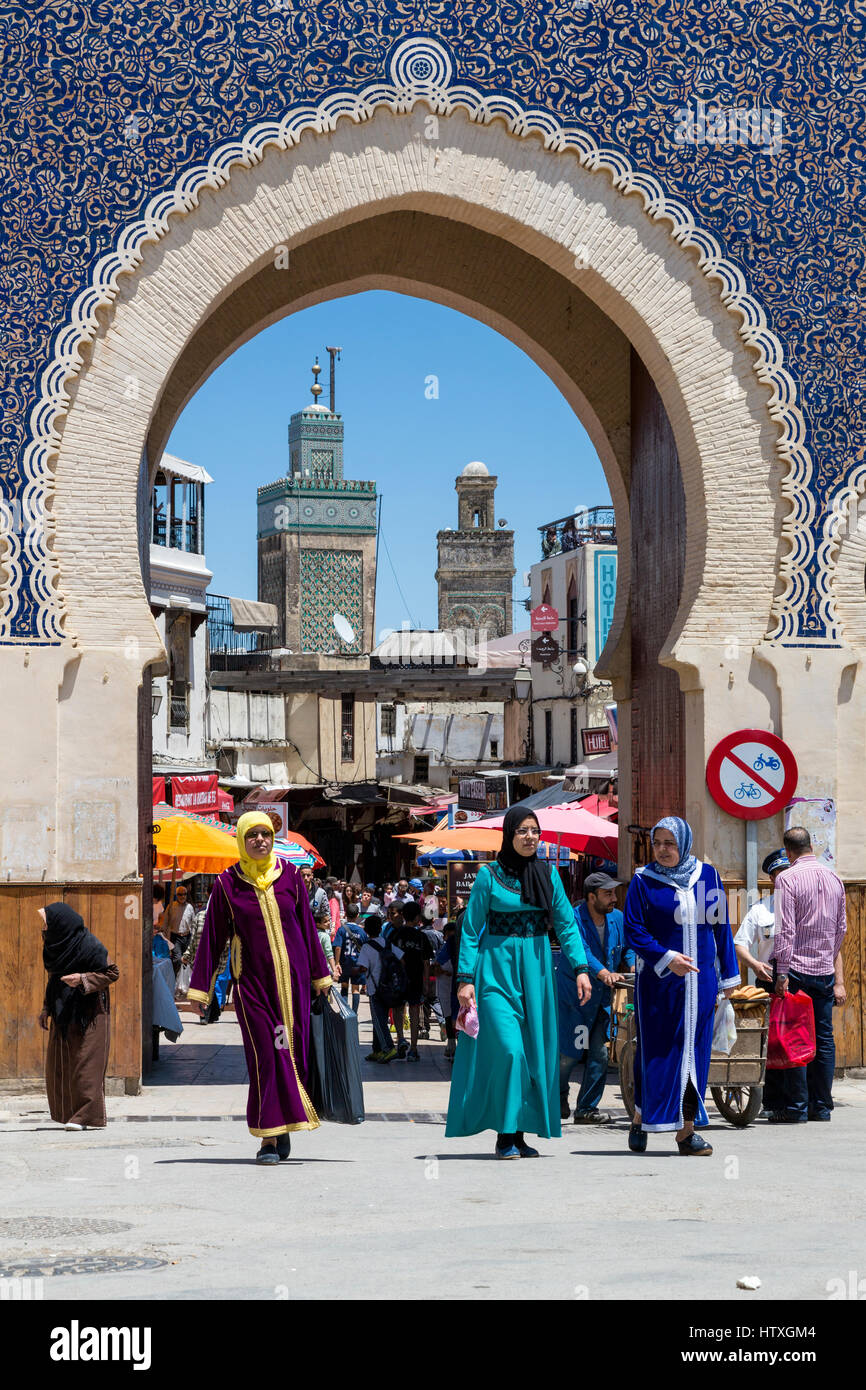 Fes, Morocco.  Bab Boujeloud, Women in Colorful Djellabas and Headscarfs Exiting Fes El-Bali, the Old City.  The minaret of the Bou Inania medersa is  Stock Photo