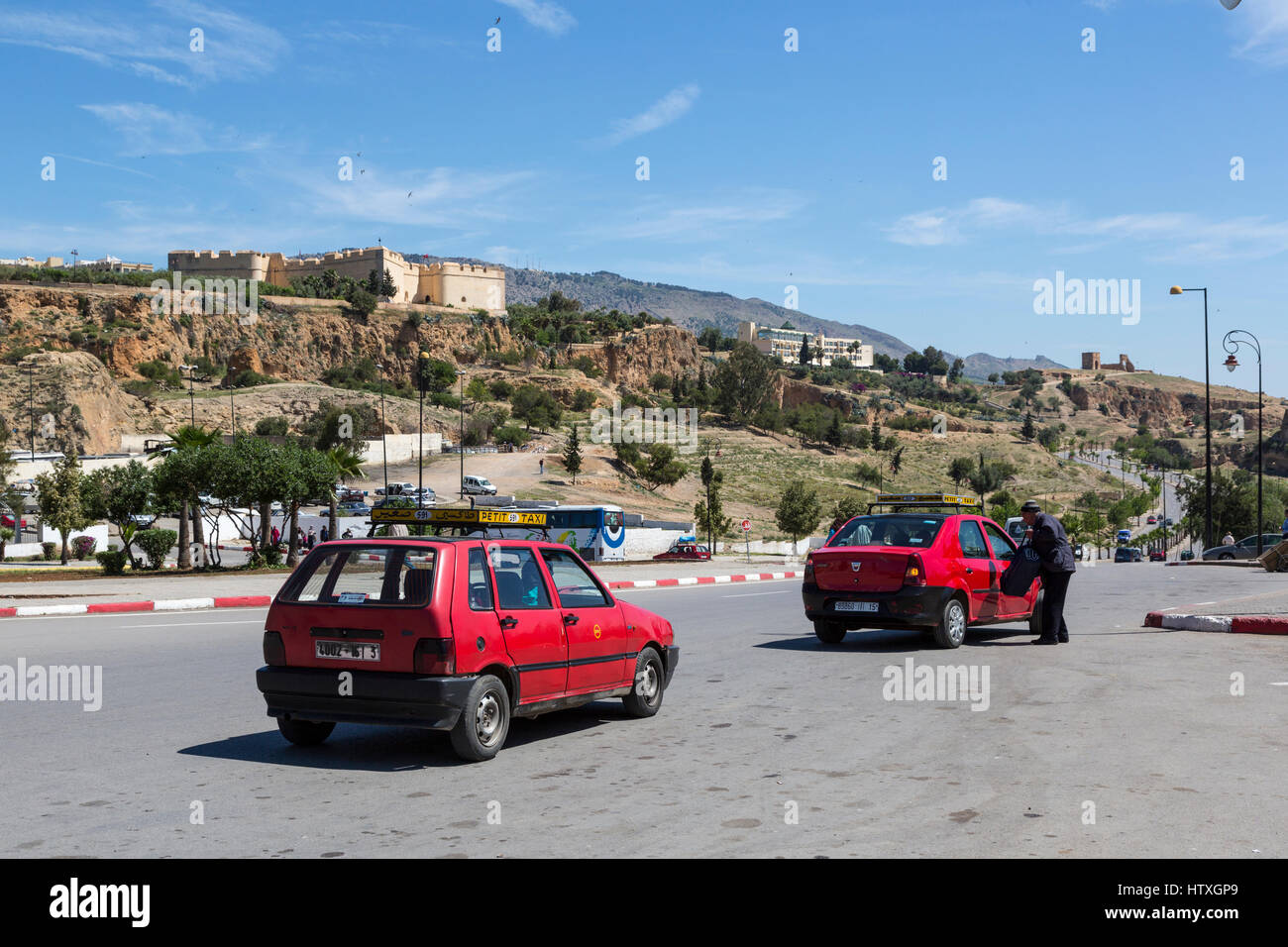 Fes, Morocco.  Taxis Outside the Bab Mahrouk.  Borj Nord on the Hillside, on left; Hotel les Merinides in center, Merenide Tombs on far right. Stock Photo