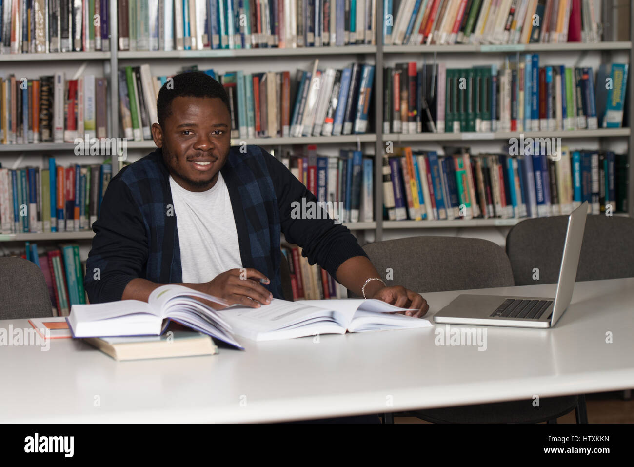 In The Library - Handsome African Male Student With Laptop And Books Working In A High School - University Library - Shallow Depth Of Field Stock Photo