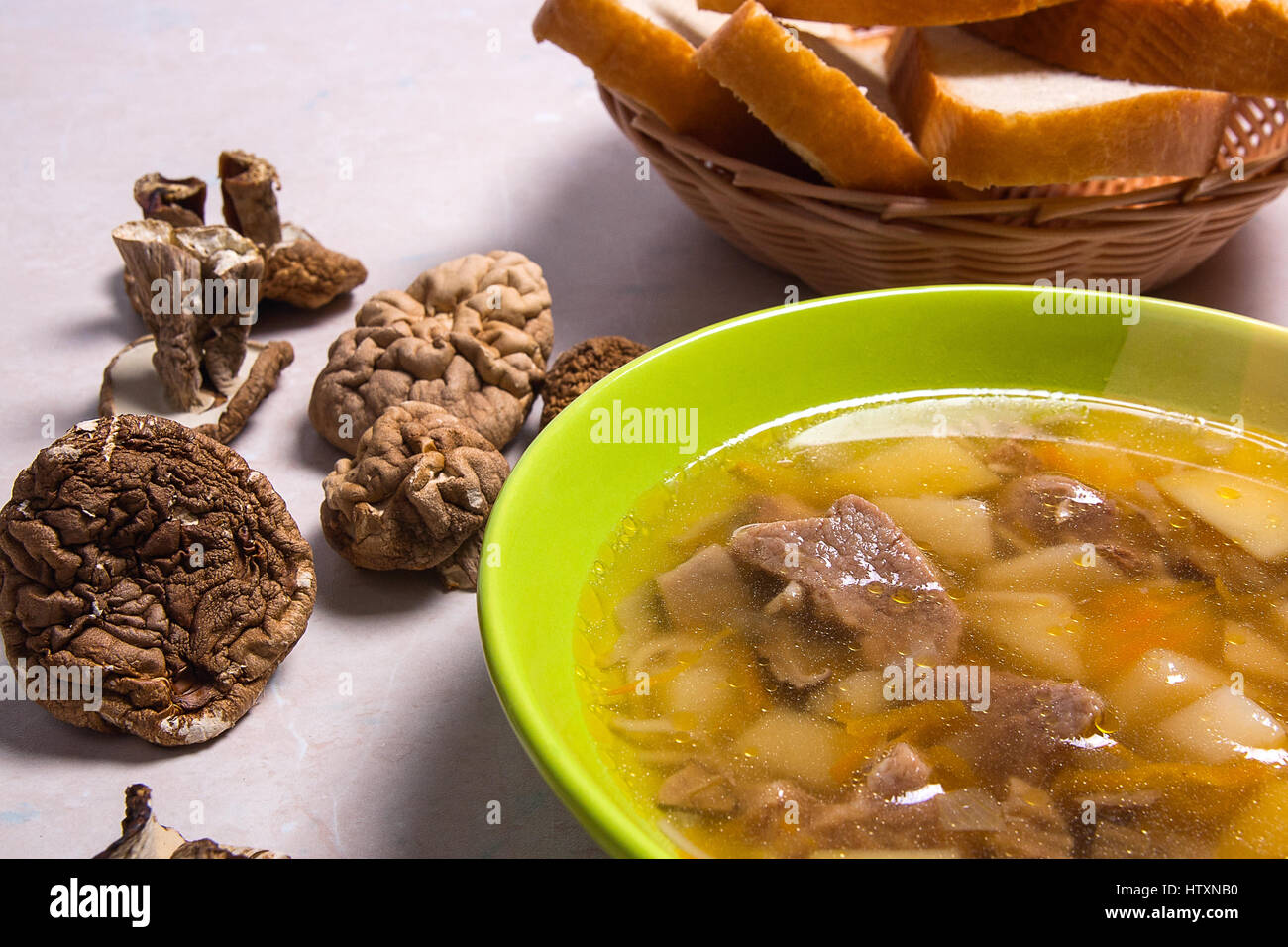 Mushroom soup in green plate on a light stone background. Several dried porcini or white  wild mushrooms on brown cloth. Slices of white bread in bask Stock Photo