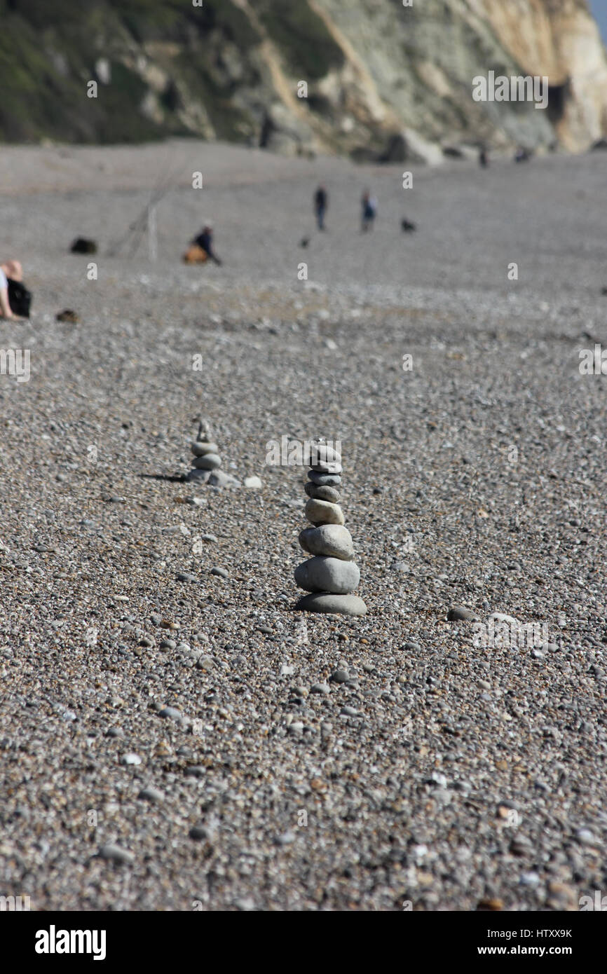 A cairn of pebbles arranged on Branscombe beach, Devon, with another cairn of arranged pebbles behind on a sunny day Stock Photo