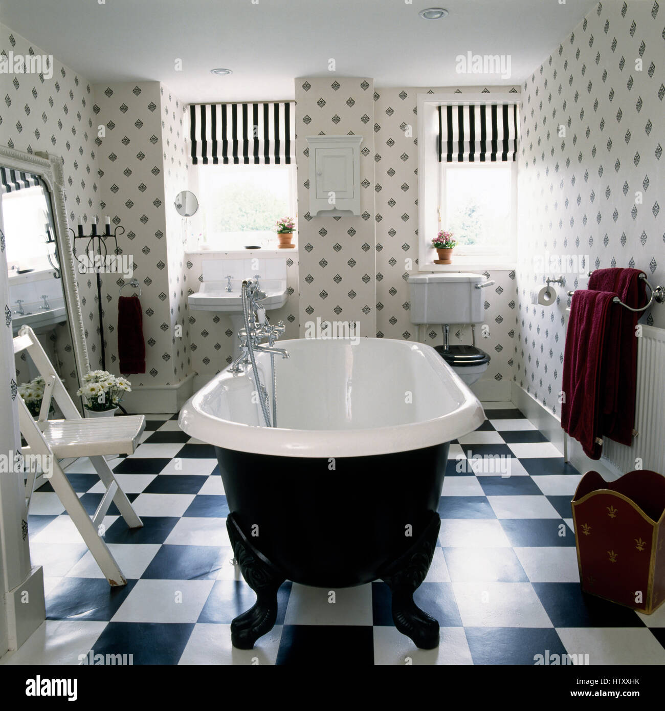 Roll top bath and black+white chequer board floor in a black and white bathroom with a simple stenciled pattern on the walls Stock Photo