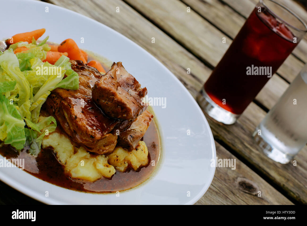 Lamb shank with vegetables on an pub outdoor wooden table Stock Photo