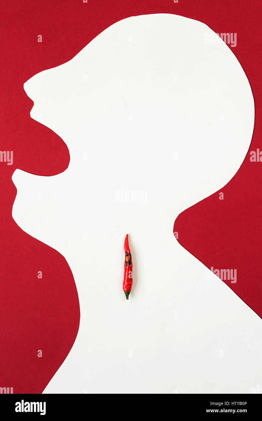 the contour of the person cut from white paper on a red background with an open mouth and hot red pepper lying inside him. cold concept, sore throat, burning in a throat, top view, flat lay. Stock Photo